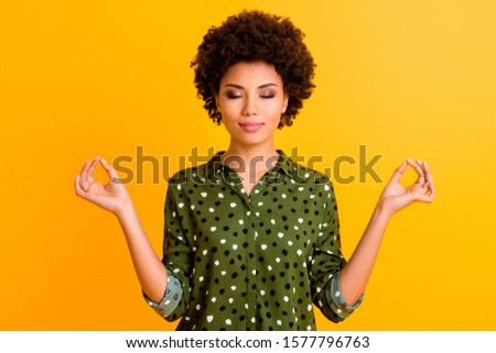 Photo of beautiful dark skin lady eyes closed holding hands om position meditating morning relaxation wear green dotted shirt isolated yellow color background
