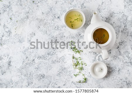 Herbal tea in white teapot and white bowl on and thyme stalks light textured background,  top view, copy space Royalty-Free Stock Photo #1577805874