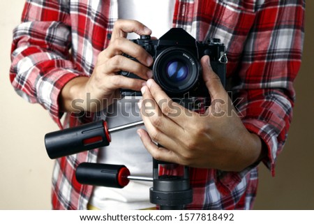 Photo of an adult man holding an old and vintage small format or 135mm film camera on a tripod.