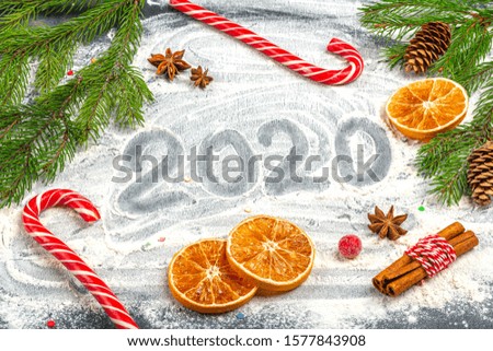 Christmas flat lay composition. 2020 inscription and frame of fir branches, cones, star anise, cinnamon and dried oranges on a flour background. Christmas, winter holidays, new year concept. 