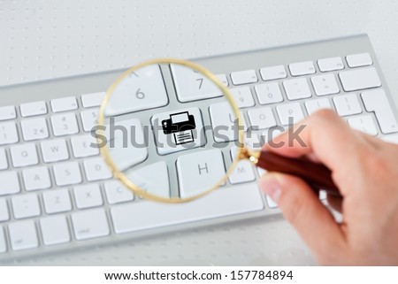 Close-up of hand looking at printer key through magnifying glass