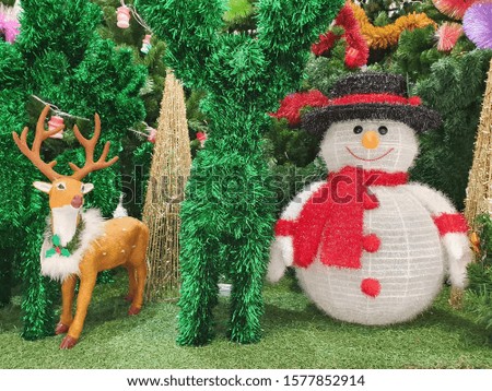 The Christmas season is decorated with snow man dolls, brown reindeer, colorful rainbow and mock-up Christmas trees in green grass.