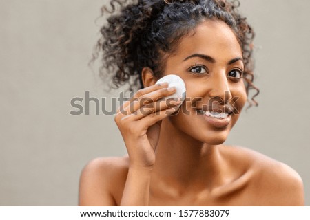 Young pretty african american woman taking off makeup with cotton wipe sponge. Smiling girl cleaning face isolated over background. Black young woman cleansing face, daily healthy beauty routine. Royalty-Free Stock Photo #1577883079
