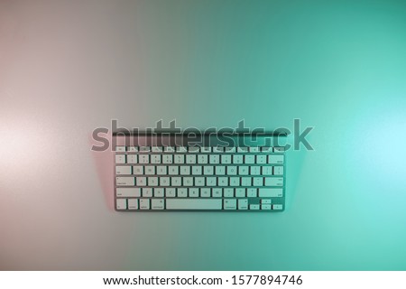 Beautiful modern silver keyboard in the color light on a table and night background. Top view.