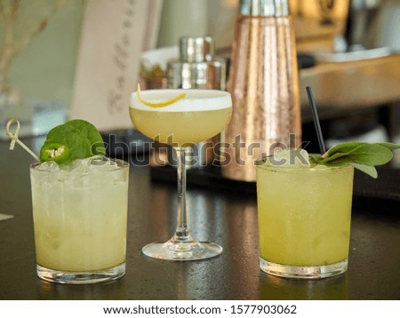 Three yellow colored cocktail drinks on a bar counter, copper shakers on a background 