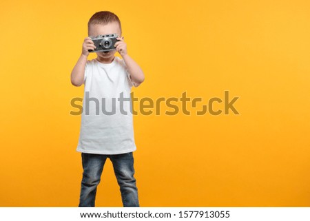 Boy taking a picture with a retro camera over yellow background