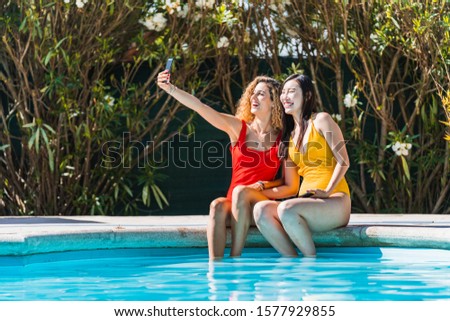 Stock photo of girls of different ethnic groups sitting at the edge of the pool and making a selfie