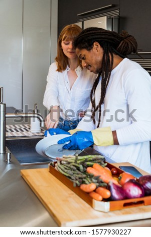 Stock vertical photo of a multicultural couple and the boy is cleaning the dishes with rubber gloves. Lifestyle