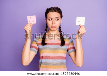 Photo of gloomy lady holding paper emoticons good and bad mood prefer negative emotions awful day wear casual striped t-shirt isolated pastel purple color background