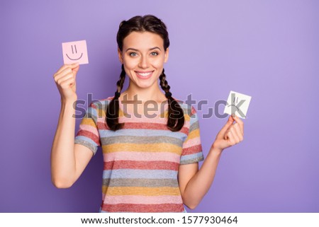 Photo of funny lady holding paper emoticons good and bad mood recommending positive emotions wear casual striped t-shirt isolated pastel purple color background