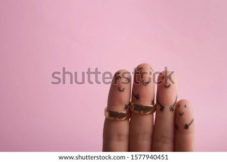 Painted happy fingers smiling in love against pink background with copy space for ad text. Marriage wedding rings