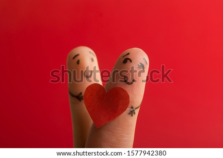 Valentines day fall in love concept. Painted happy funny fingers smiley holding red heart against red background with copy space for ad text