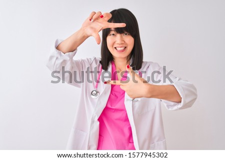 Young beautiful chinese doctor woman wearing stethoscope over isolated white background smiling making frame with hands and fingers with happy face. Creativity and photography concept.