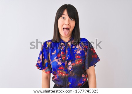 Young beautiful chinese woman wearing summer floral t-shirt over isolated white background sticking tongue out happy with funny expression. Emotion concept.