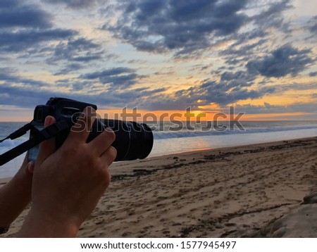 hand of a person with a camera on a beach at sunset
