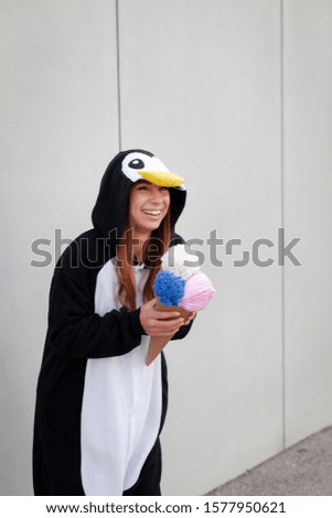 beautiful, young woman in penguin costume is eating deco ice cream in front of concrete wall