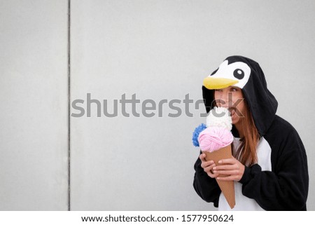 beautiful, young woman in penguin costume is eating deco ice cream in front of concrete wall