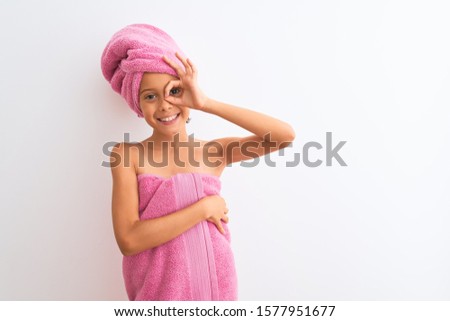 Beautiful child girl wearing shower towel after bath standing over isolated white background doing ok gesture with hand smiling, eye looking through fingers with happy face.