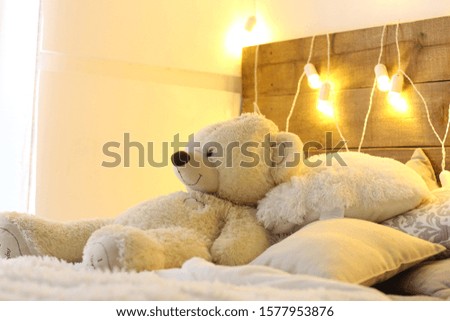 white bed with teddy bear with christmas garland light decoration close up photo