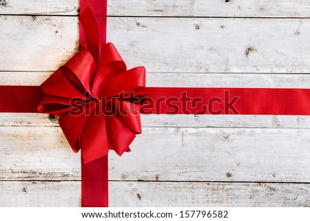 Colourful red Christmas ribbon tied with an ornamental bow on weathered white painted wood with copyspace for your seasonal greeting