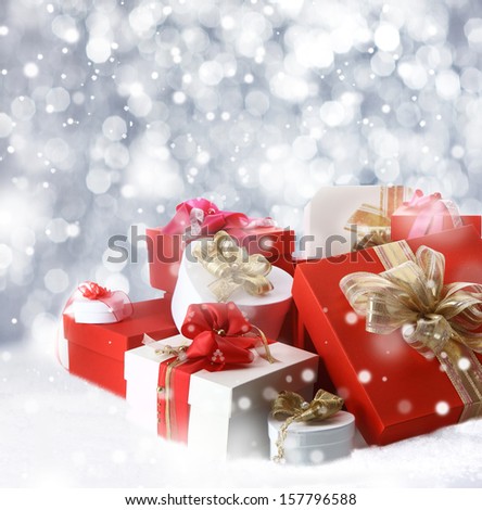 Beautiful collection of red, white and gold decorated Christmas gifts in all shapes and sizes standing in a bed of fresh winter snow surrounded by falling snowflakes
