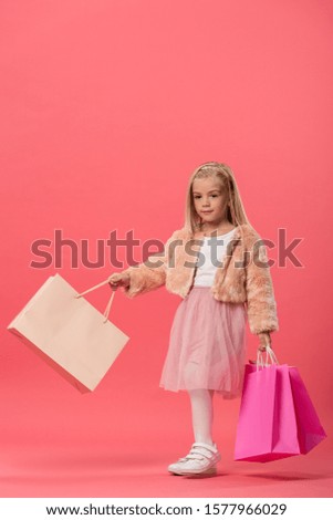 cute kid holding shopping bags on pink background with copy space  
