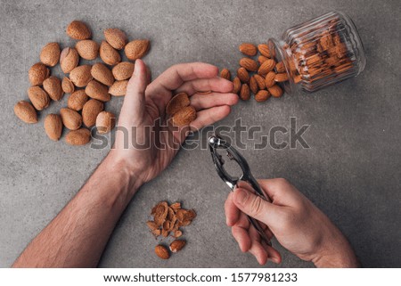 Male hands chop almonds. Whole and peeled almonds on a stone surface. Gray background. Top view.