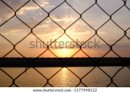 Sunset behind a wire fence near an artificial lake