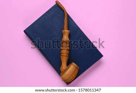 Vintage style. Old book, smoking pipe on pink background. Top view, minimalism