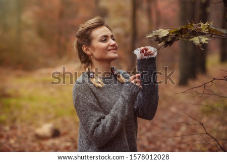 Attractive woman with braided pigtails holds fallen leaves in her hands in the autumn forest. Autumn art portrait