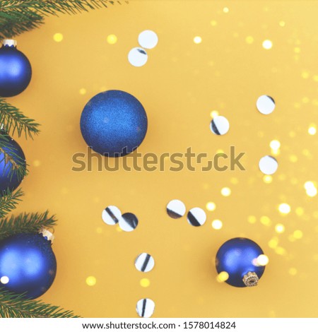 Christmas tree branch decorated with blue toys on an orange background.