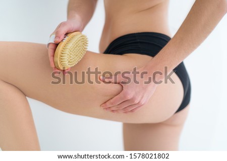 Woman brushing skin buttocks and butt with a dry wooden brush to prevent and treatment cellulite and body problem after shower in bathroom at home. Skin health