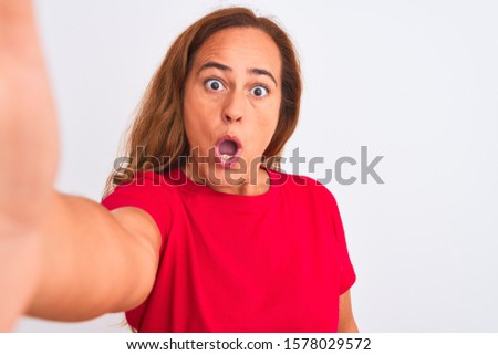 Middle age mature woman taking a selfie photo using smartphone over isolated background scared in shock with a surprise face, afraid and excited with fear expression
