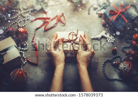 Christmas New Year concept top view. Unrecognizable woman wrapping draws a gift box on wooden table, point of view