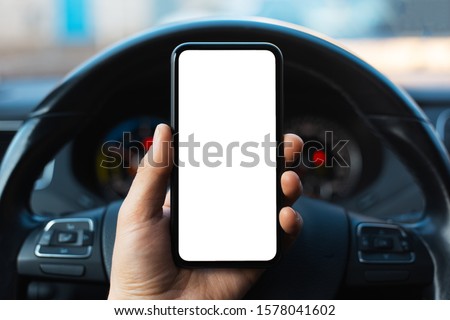 Close-up of male hand holding smartphone with white mockup on screen, background of car steering wheel. Royalty-Free Stock Photo #1578041602