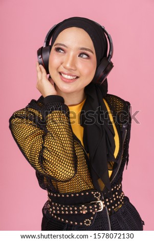 Beautiful young hipster girl wearing  hijab and listening to music with wireless headphones isolated over pink background. Technology in a modern lifestyle concept.