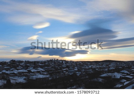 Sunset in a small town with an animal-like cloud. Silhouette of a winter city with beautiful blue sunset and white clouds. Artistically blurry