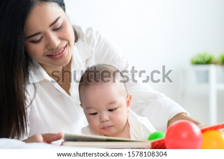 Mother and baby relation or lovely family concept : Portrait photo of Asian mother reading and teaching her baby in bed.