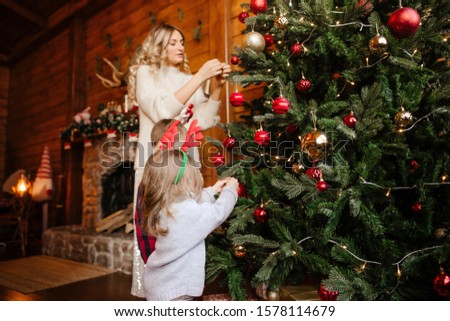 Mom and kids hang Christmas tree toys on the Christmas tree decorating the house