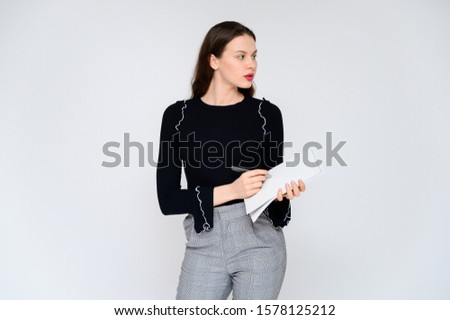 Concept adult girl on a white background with a white folder in hands. A photo of a pretty brunette girl in gray trousers and a black sweater smiles and shows different emotions in different poses.