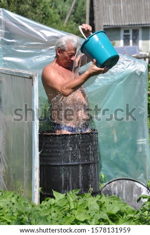 A man is standing in a barrel of water and doused with cold water from a bucket.