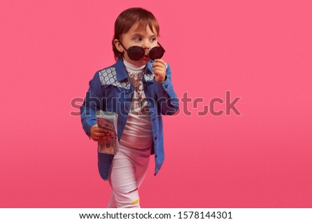 A little fashion girl holding dollars on pink background