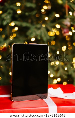 Digital tablet computer with isolated screen on the background of the Christmas tree, bokeh and garland.
New year gift
Place for text. Copy space