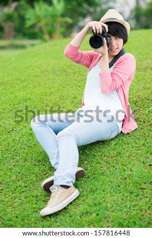 Vertical image of a freelance photographer in the process of photo making on the grass in the park on the foreground