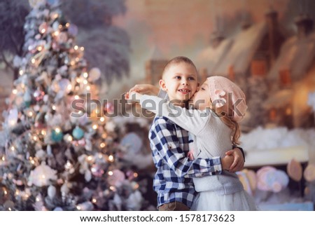 happy kids, a boy and a girl of 6-7 years old, on Christmas tree in bright colors, with a New Year tree on the background of fabulous houses and sweets, hugging