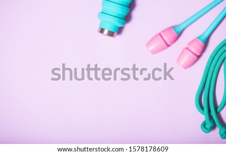 skipping rope, rhythmic gymnastics clubs and a blue water bottle on a purple background