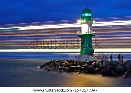 Lighthouse at the entrance of the port of Warnemünde, Rostock, in Northern Germany, at the Baltic Sea; lightbeams of a cruiseship, passing the lighthouse. 