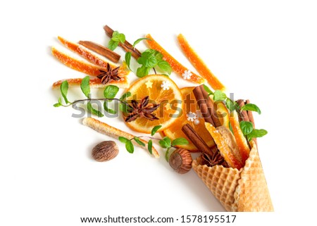 Christmas composition of candied orange peel, cinnamon sticks, nuts and mint in a waffle cone on a white background