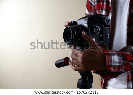 Photo of an adult man holding an old and vintage medium format film camera on a tripod.