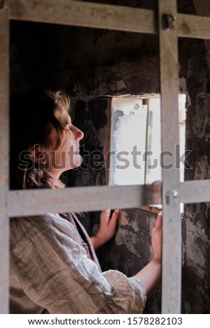 Woman in vintage clothes at window behind prison bars. Retro style costume on Halloween